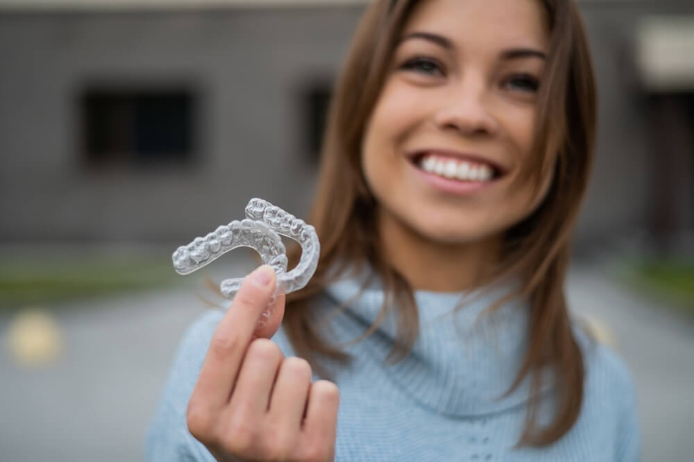 Caucasian woman with white smile holding transparent removable retainer